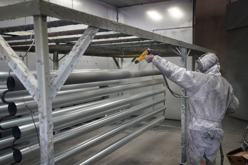Industrial technician in white protective coveralls spray cleaning steel pipe racking