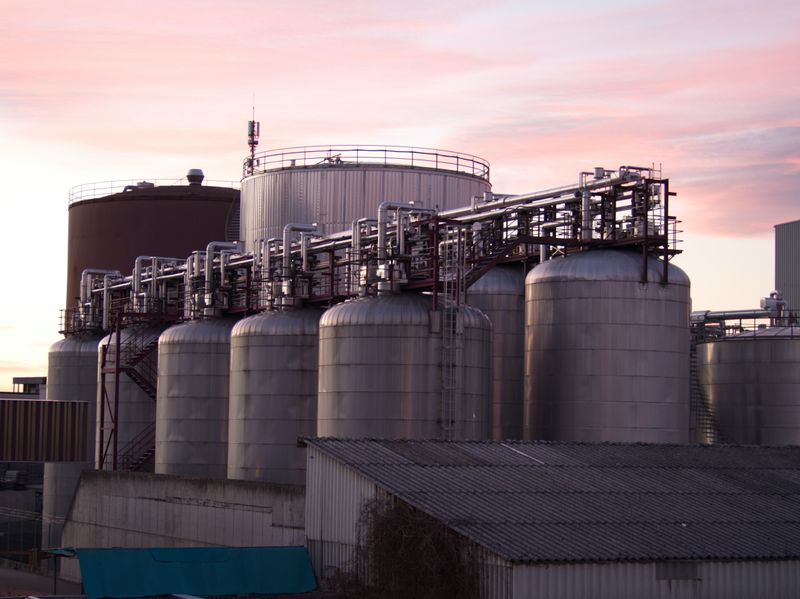 Industrial refinery with large stainless steel storage tanks connected by piping infrastructure at sunset