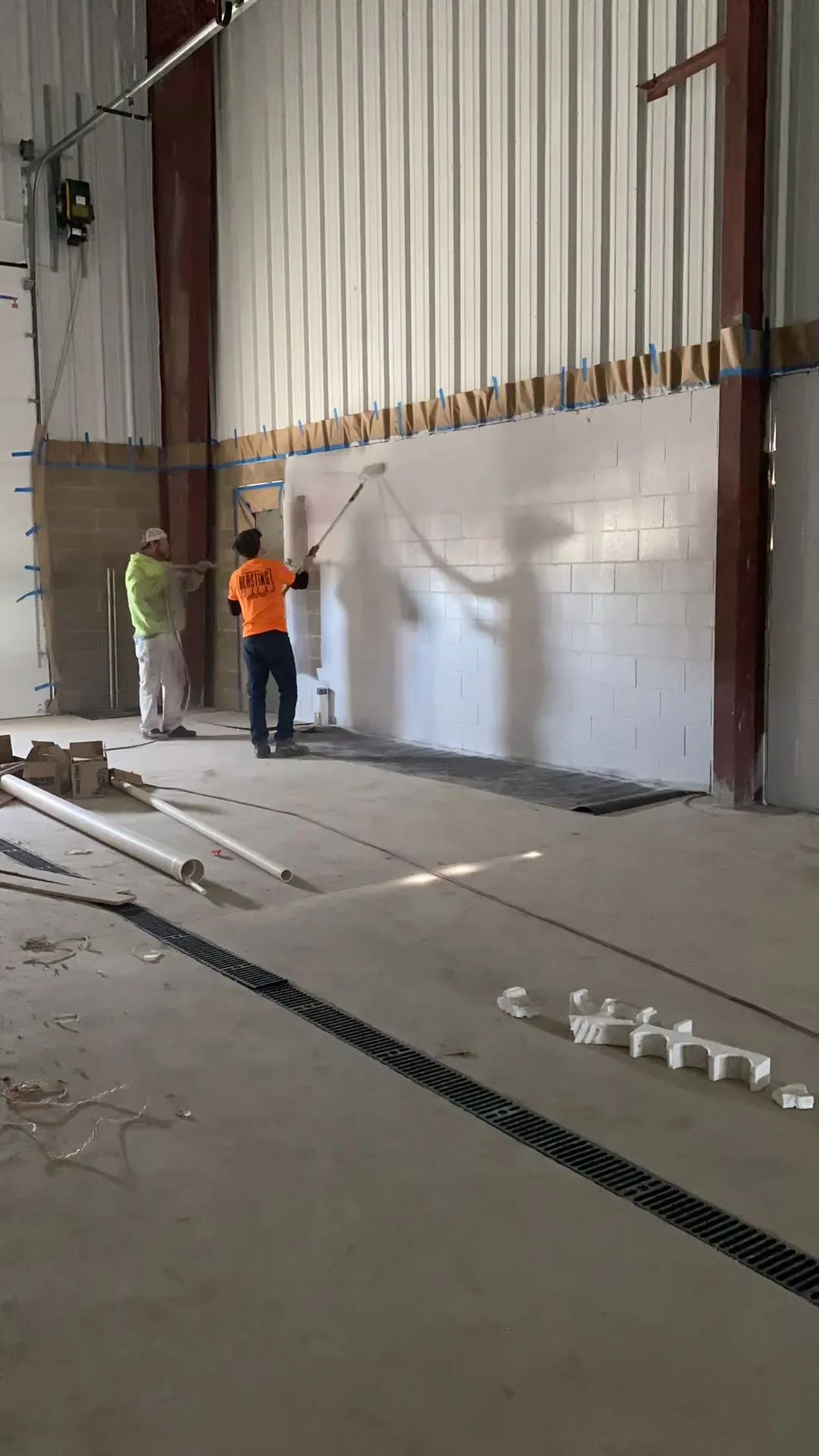 Two-man crew applying block filler by roller — wall partially filled showing the before-and-after difference in one shot
