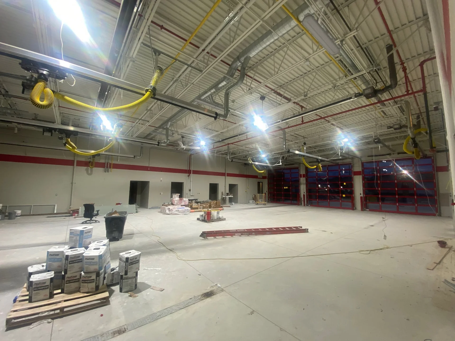Wide interior view of the apparatus bay with red accent stripe and materials staged for new construction paint work