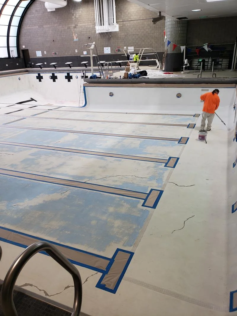 Crew applying the new coating system to the pool wall, base coat visible on the floor