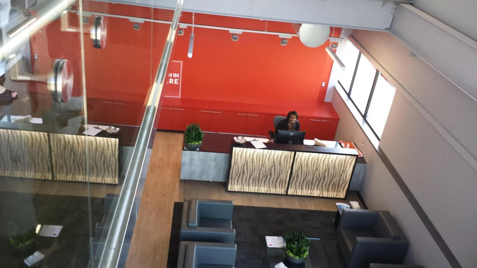 Office reception area viewed from above, with bold red accent wall and reception desk
