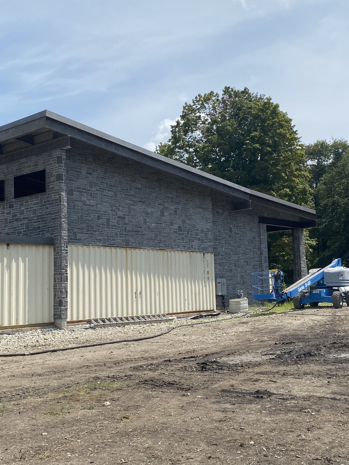 Side view of container house with stone facade and boom lift on site