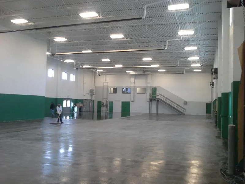 Environmental recycling facility interior with freshly painted white walls, green accent base, and exposed steel deck ceiling