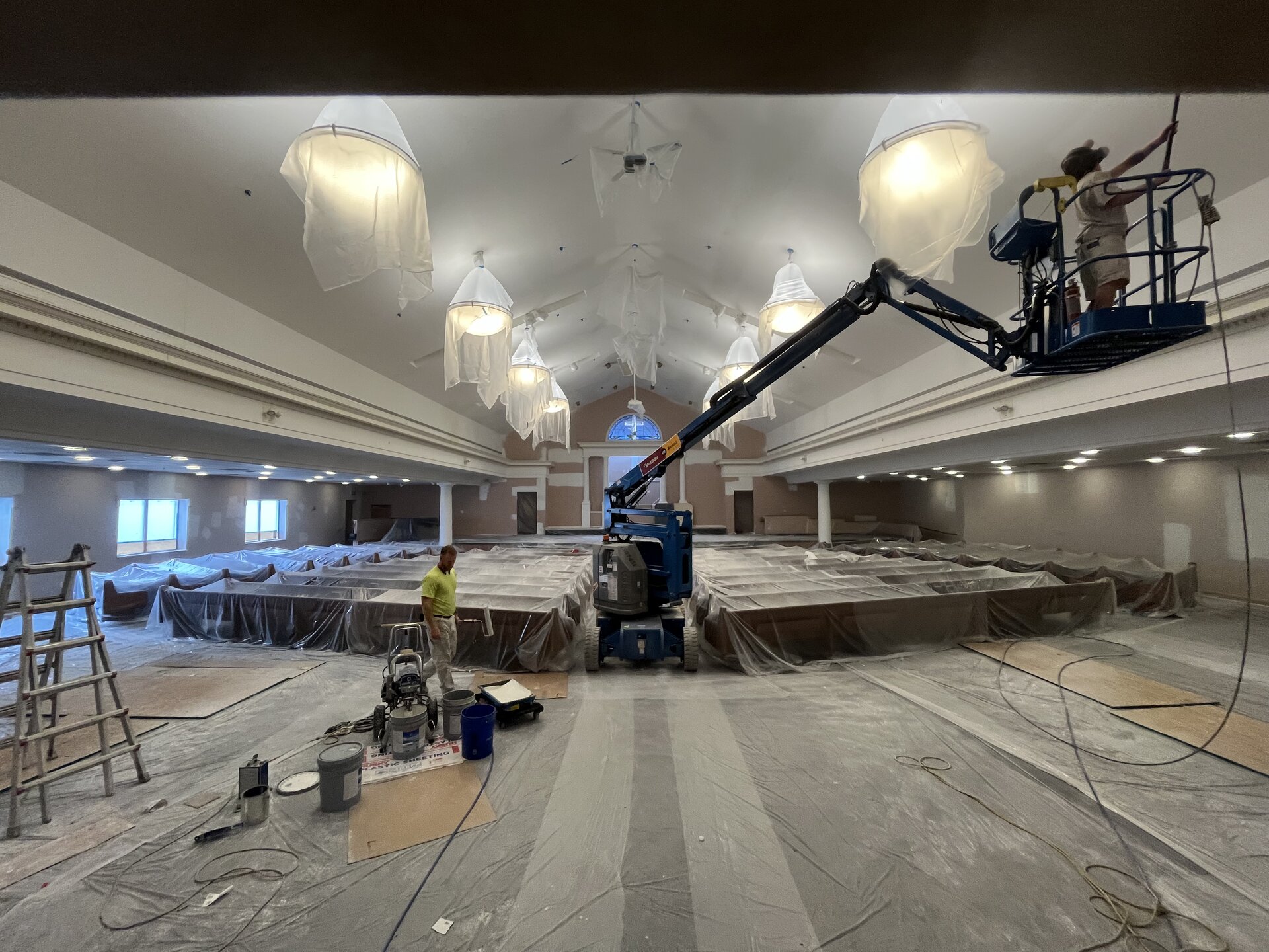 Church auditorium interior during repaint — crew painting vaulted ceiling