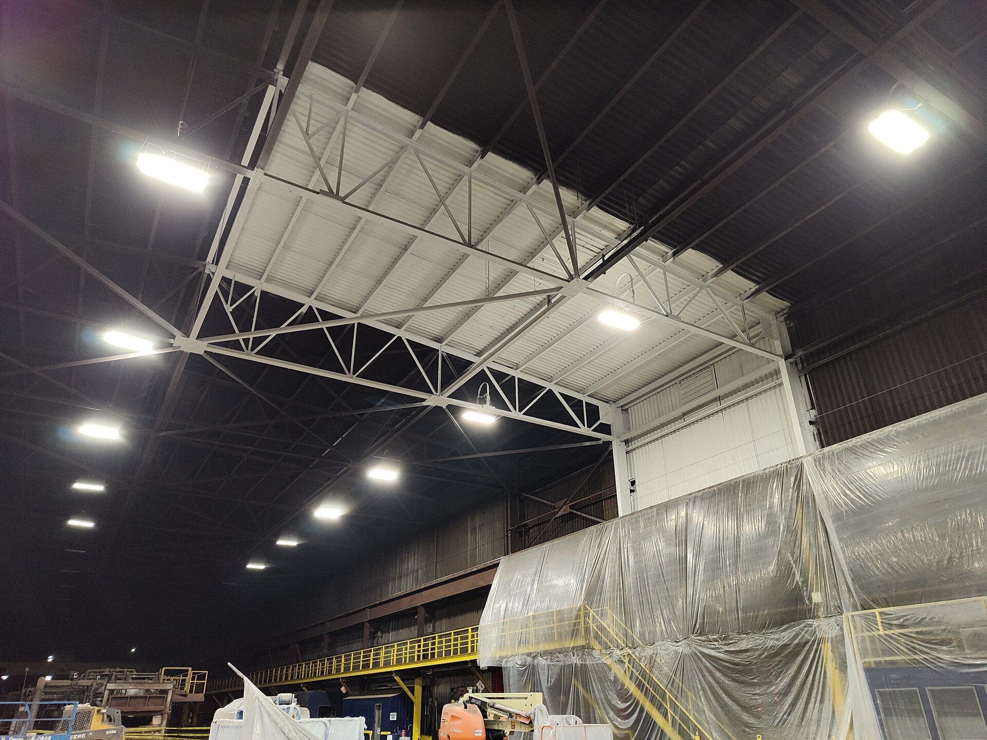 Steel mill paint sample — freshly painted white roof trusses against decades of dark unpainted structure