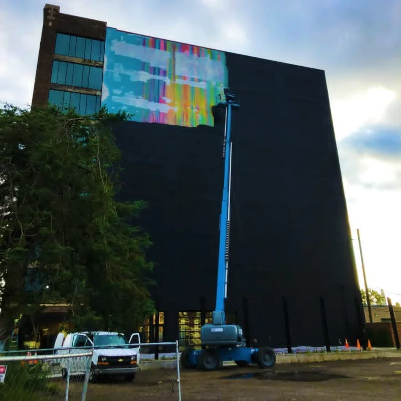 Boom lift raised along a multi-story wall as the crew covers the existing mural with black paint
