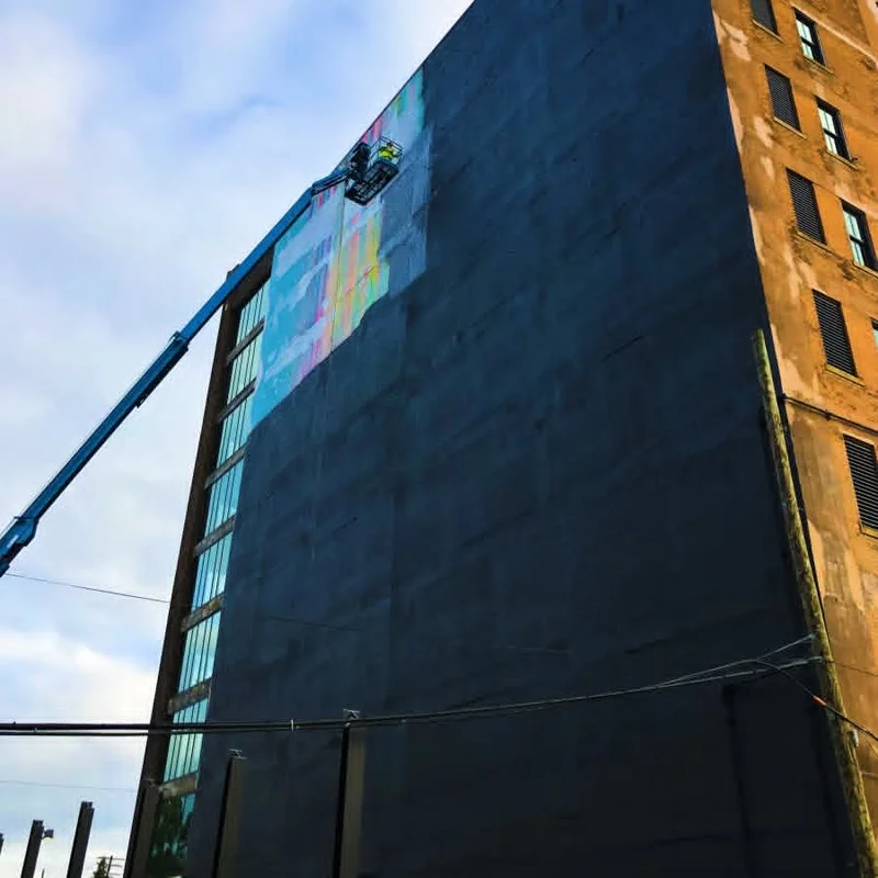 Crew in a boom lift basket rolling black base coat over the old mural high on the building