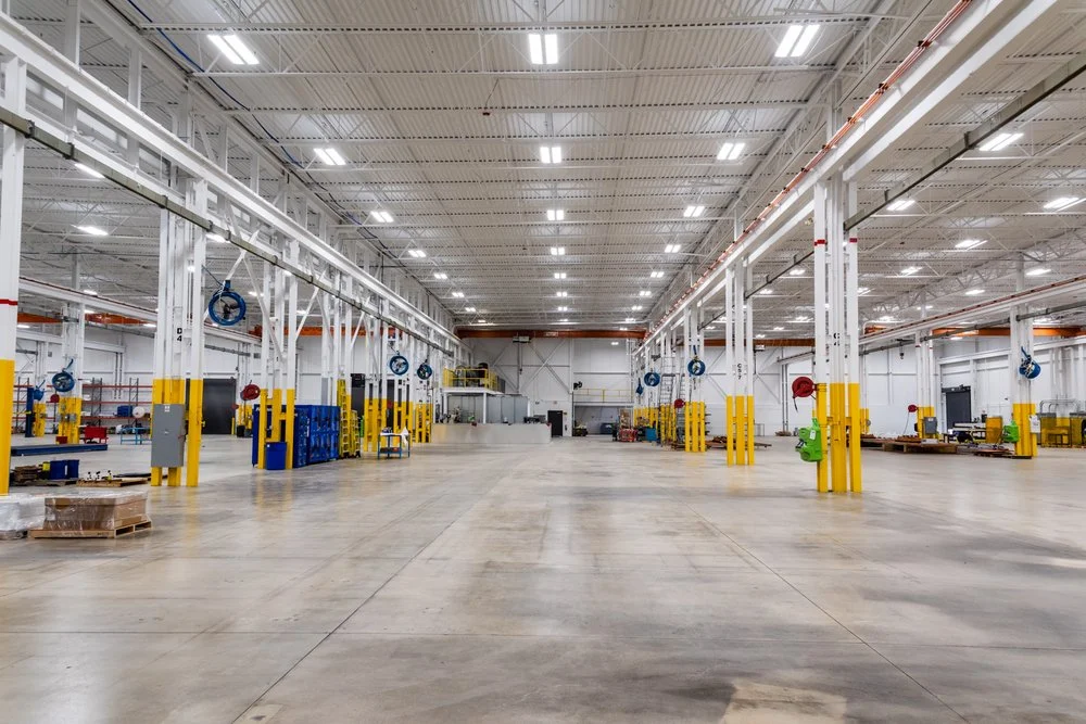 Bright, freshly painted industrial warehouse — white deck ceiling, trusses, and columns with yellow safety-painted bases over a clean open floor