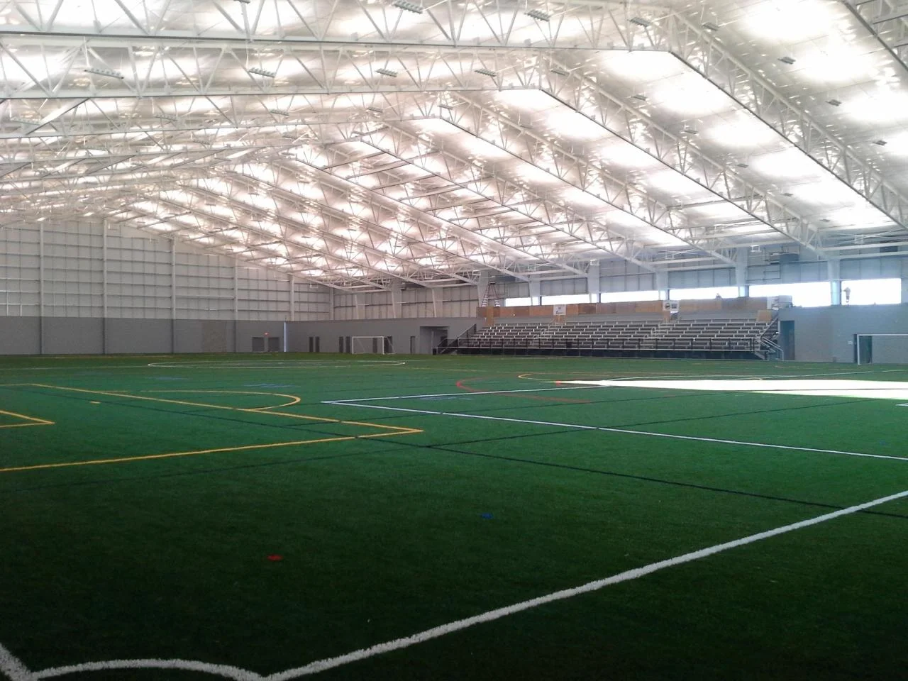 Legacy Fieldhouse interior with freshly painted white exposed steel roof trusses above the indoor turf field and bleacher seating