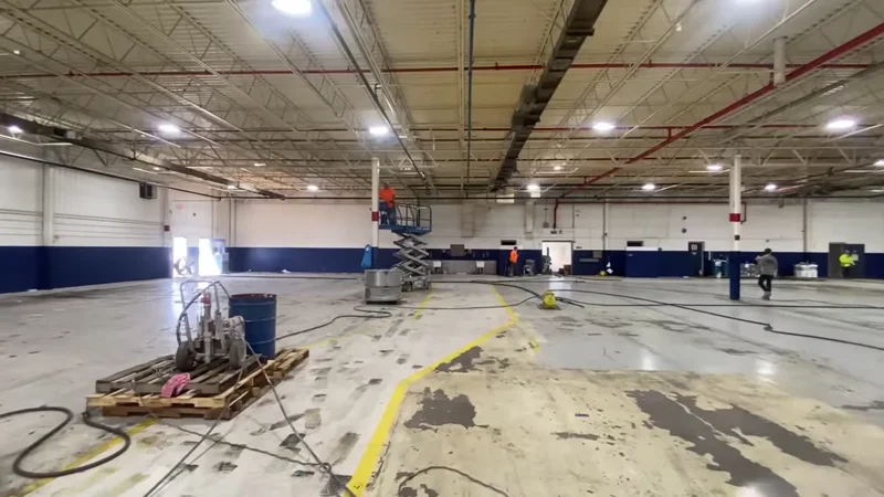 LuxWall production area during work — scissor lifts, spray rig, and plastic containment on the floor