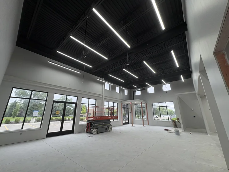 High black open-deck ceiling with exposed joists over a repainted commercial showroom space with floor-to-ceiling windows