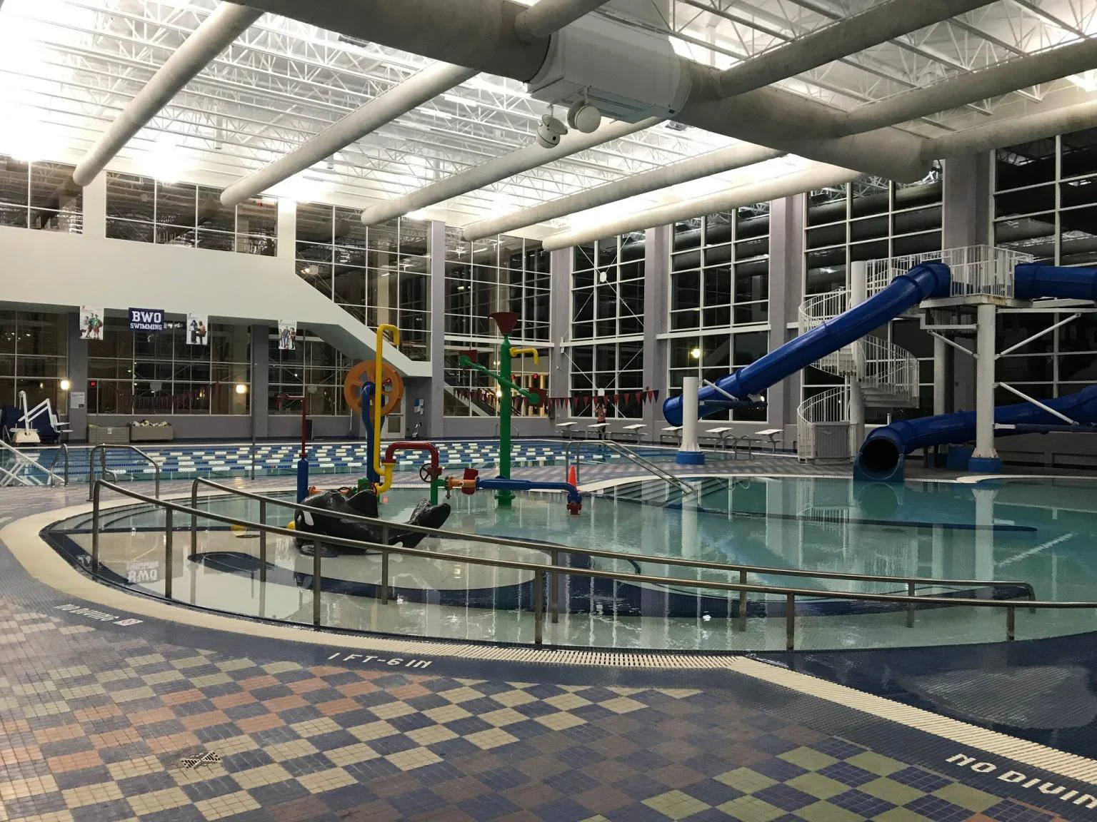 Indoor natatorium pool deck with waterslides and freshly painted overhead structure