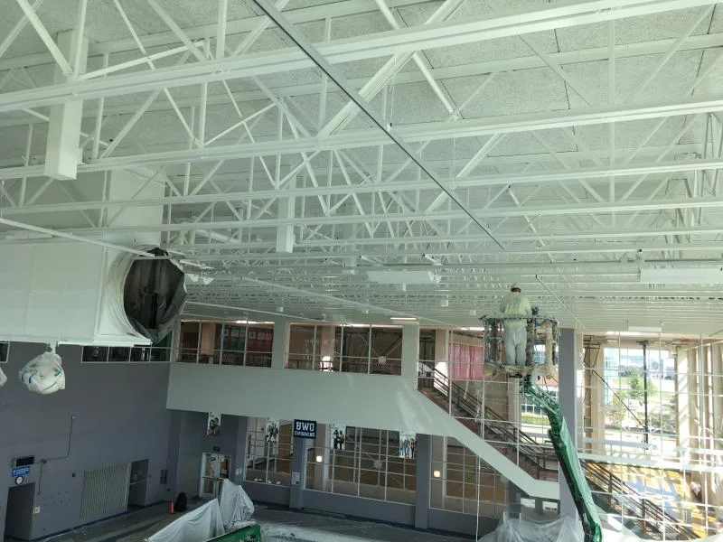 Crew on an aerial lift painting the exposed steel roof structure above the pool deck