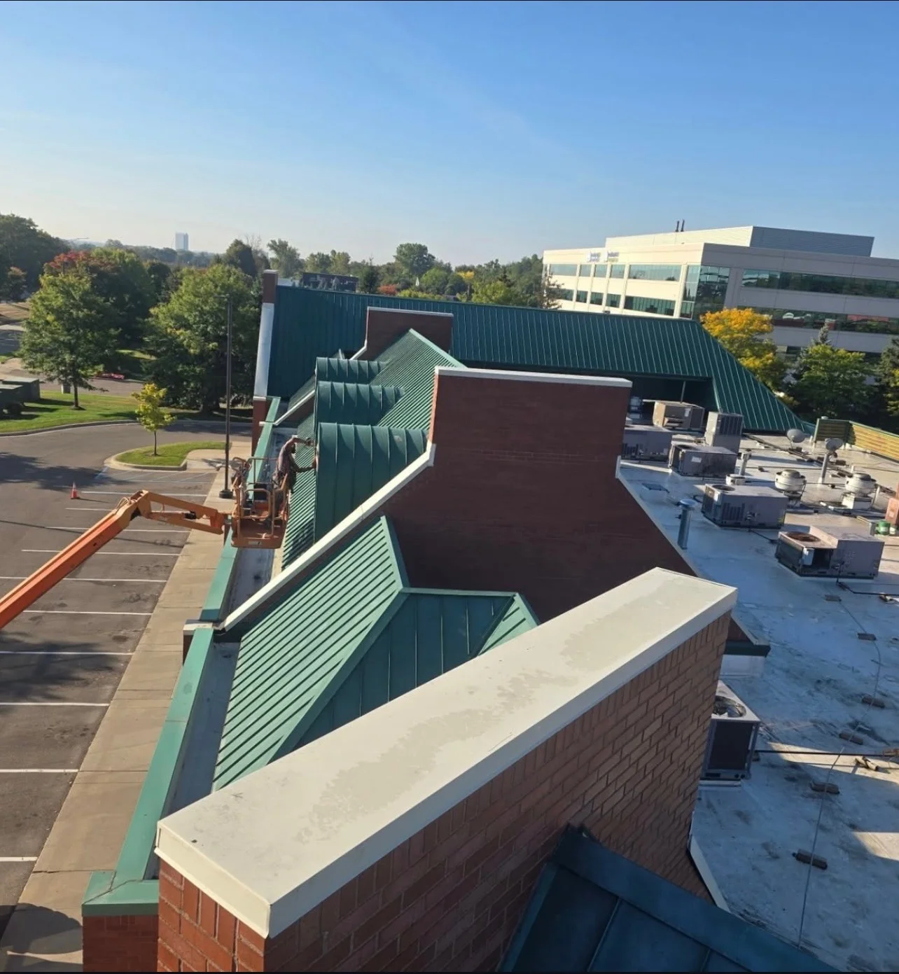 Crew on a boom lift cleaning and repainting the standing-seam metal roof and parapet caps of a shopping center
