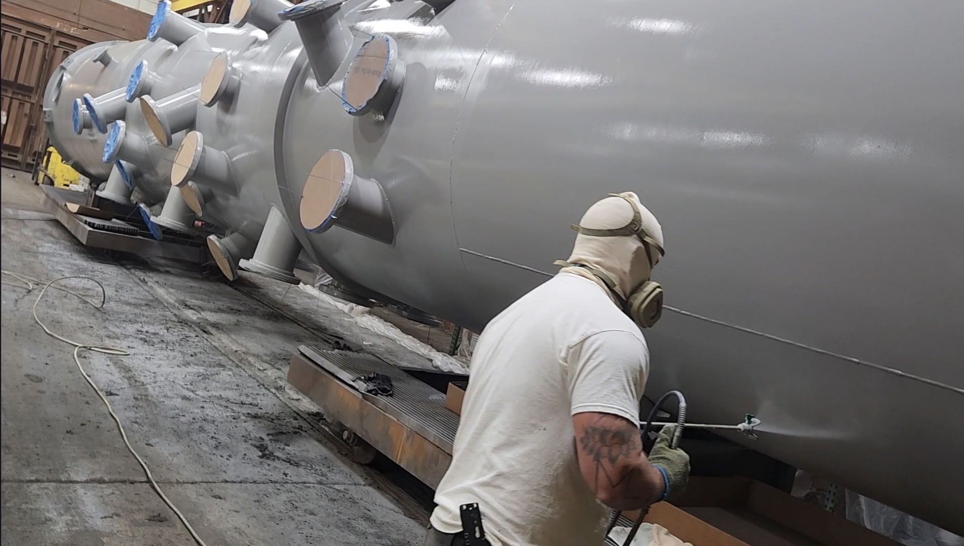 Technician spray applying specialty coating to exterior of large vessel