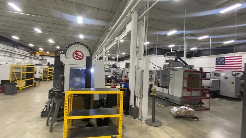 Repainted SRS Manufacturing shop floor with white columns and ceiling, CNC equipment, and American flag on the back wall