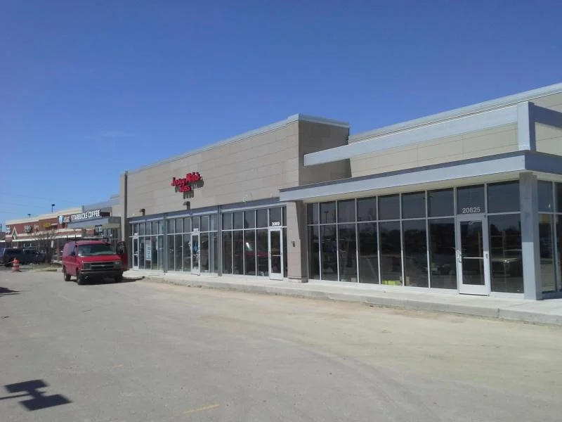 Retail strip mall exterior with freshly painted tan panel facade and dark accent trim above the storefronts