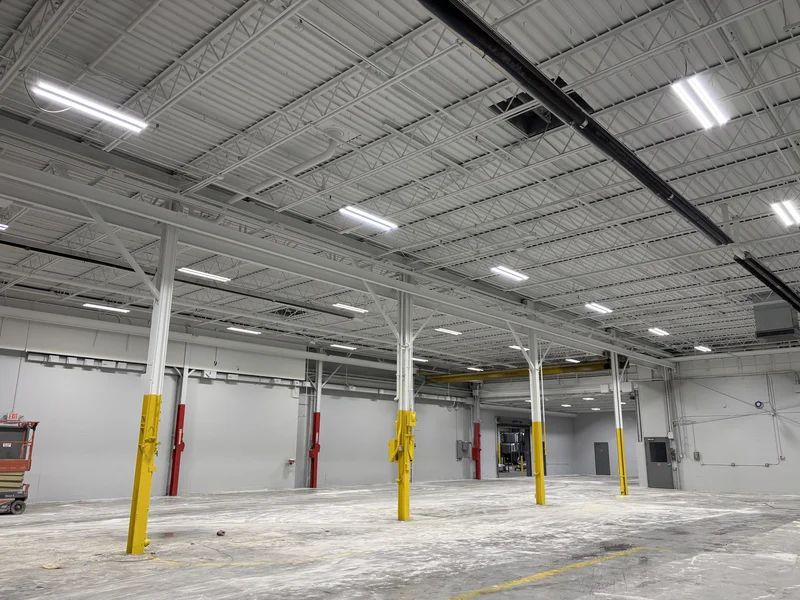 Wide view of the repainted warehouse bay — white ceiling and steel, gray walls, and yellow and red column bases