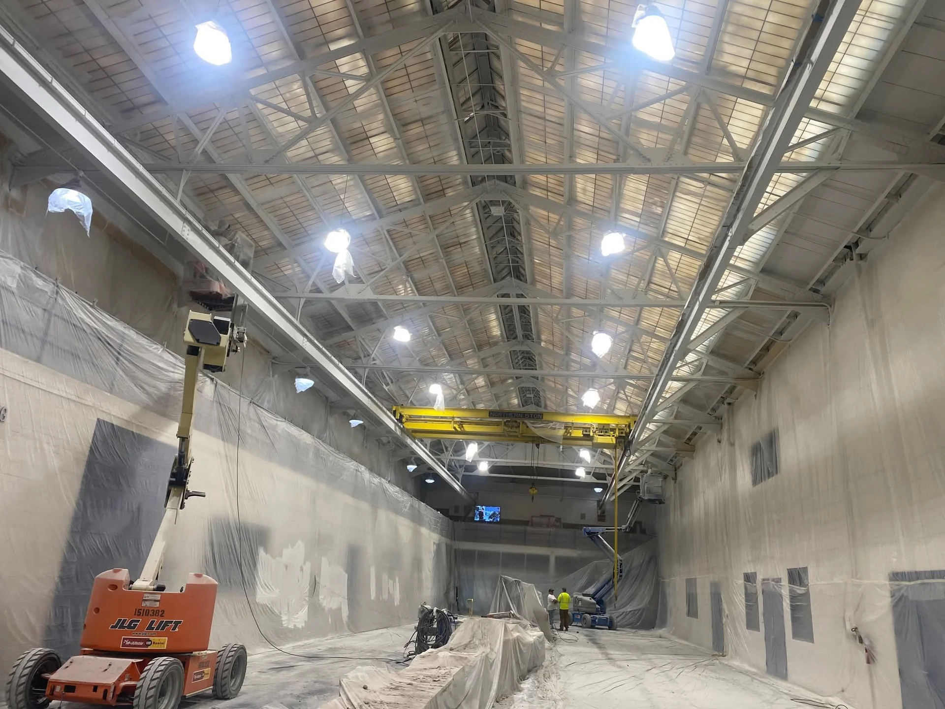 University of Detroit Mercy engineering atrium — full containment with plastic sheeting, scissor lift in place, spray painting in progress