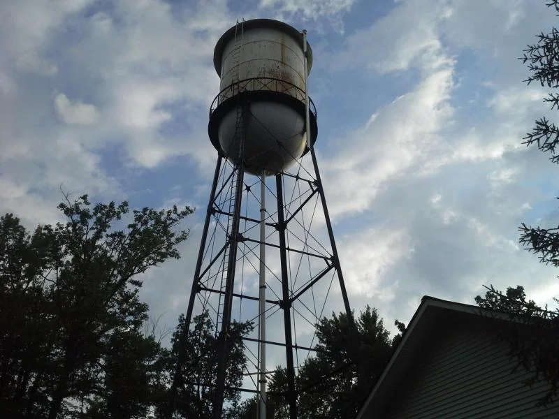 Elevated water tower before repaint, showing rust and weathered paint on the tank