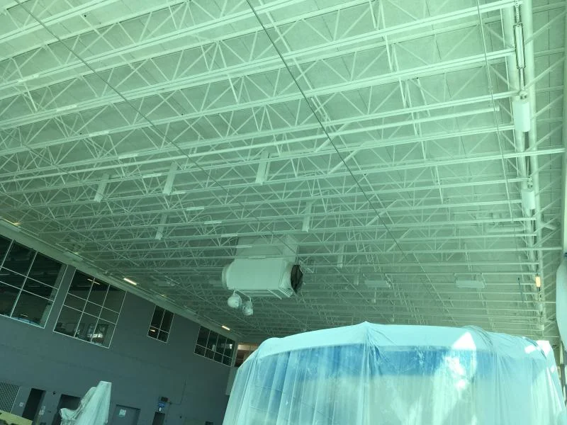 Close-up of the freshly painted white steel roof deck and trusses above the pool, with equipment wrapped for protection